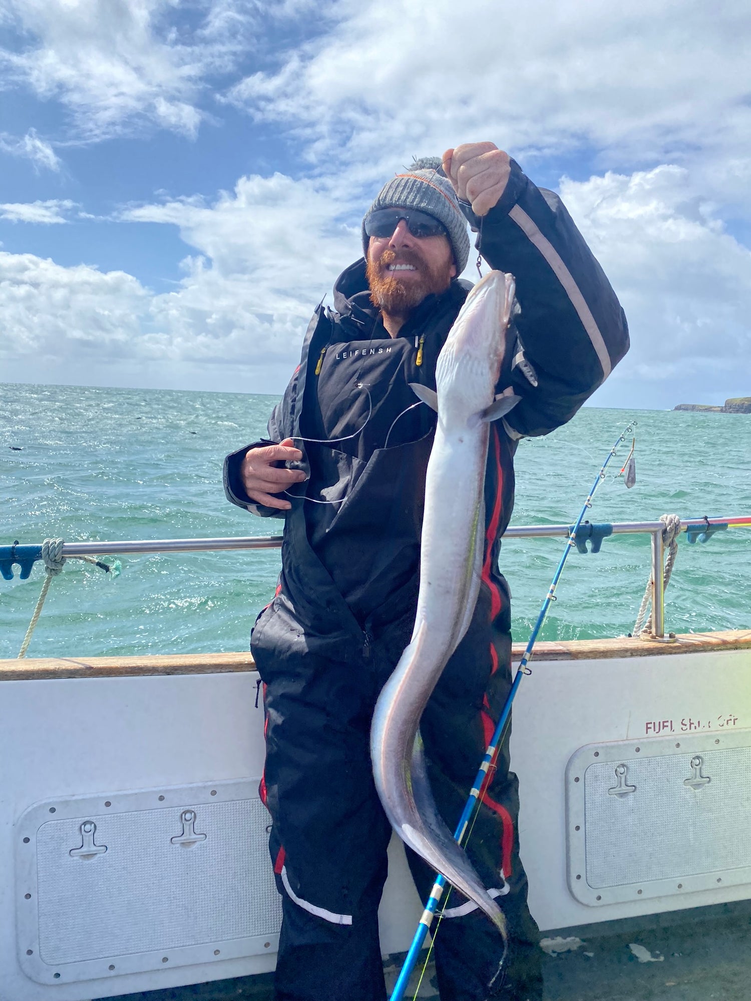 Angler holding a large eel on a fishing charter trip in Ireland with Séan Maguire, showcasing a successful catch on a boat.